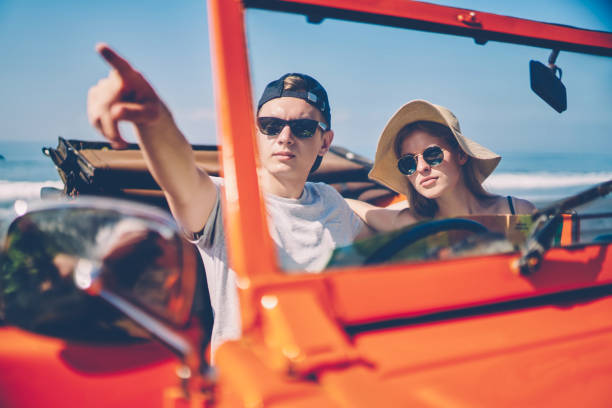 istock Hipster guy in sunglasses pointing on something discussing route for driving with girlfriend traveling together, couple in love sitting in rental car transporting on tropical island on cabriolet 1159402620