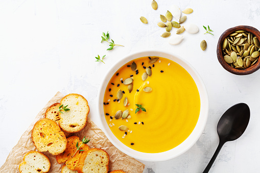 Diet autumn pumpkin or carrot cream soup in bowl served with seeds and crouton on stone table from above with copy space.