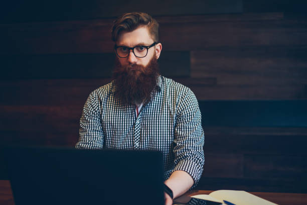 istock Half length portrait of smart bearded student in optical eyeglasses working on coursework sitting in cafe interior at digital computer device connected to wireless internet while looking at camera 1159407652