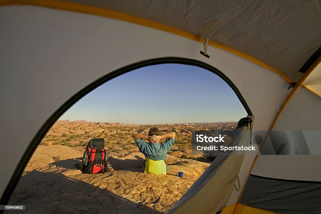 Camping in Desert of Utah Man Framed by Door of Tent Sitting with Backpack in Desert Activity Stock Photo