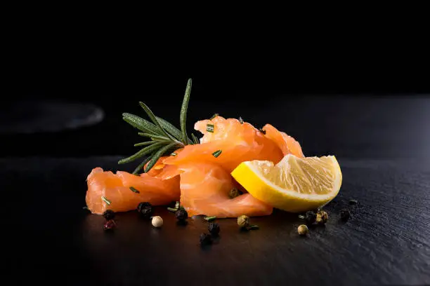 Smoked Salmon with lemon pepper and rosemary on black stone background
