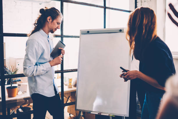istock Male and female colleagues collaborating starting work on project using flipchart for noting creative ideas, employees sharing ideas and solutions having brainstorming session in coworking office 1159410391