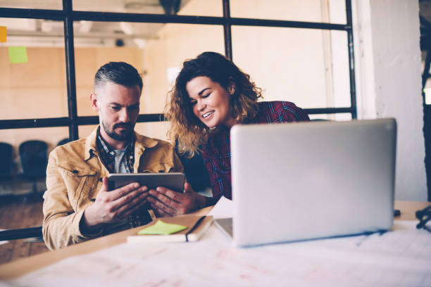 istock Young female employee watching video on digital tablet with male coach during working process, colleagues searching information for project using modern technology and wifi connection in office 1159412137