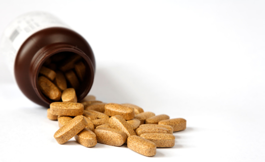 Brown vitamin pills spilling out of a bottle on white with space for copy. Shallow depth of field