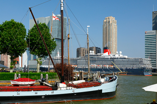 Rotterdam, Netherlands - June 26, 2019: The new harbor district of Rotterdam (Kop van Zuid) located on the south bank of the Nieuwe Maas, opposite to the city center of Rotterdam. View from the Veerhaven, a small yacht harbor - cruise ship Queen Victoria anchors at the Kop van Zuid pier.