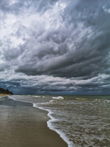 A tropical storm is about to make landfall on the beach.  The wind and waves are strong.  Above is a dramatic dark moody sky.  These storms can be violent and dangerous.  It is Monsoon season in Ko Lanta, Krabi province, Thailand.