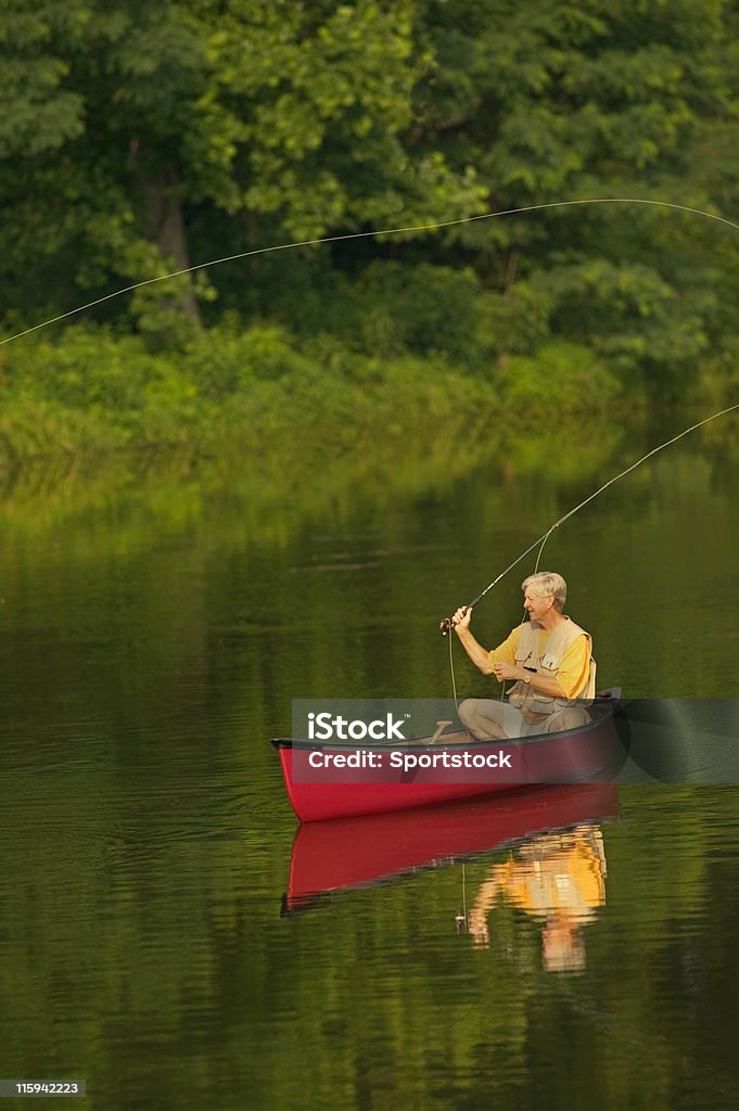Uomo anziano pesca con la mosca da canoa - Foto stock royalty-free di Adulto