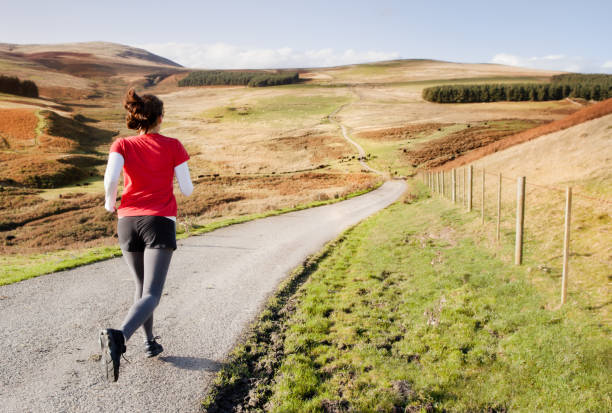 Cross Country A woman running a long distance down an empty road in the countryside. distance running stock pictures, royalty-free photos & images