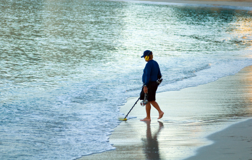 Man with a metal detector searching for lost riches on a quite beach