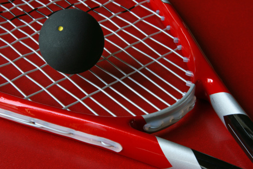 Close-up of a squash racket and a ball on a red background.