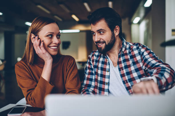 istock Two happy young freelancers having break from work on laptop computer resting at cafeteria, hipster guy looking in eyes female friend showing picture and both laughing sitting desktop netbook 1159427100