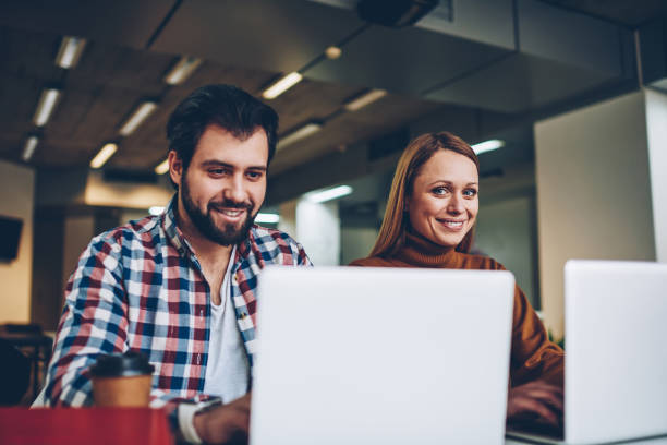 istock Two business persons working carefree togetherness on new project for social network using laptop computers connected to wifi while smiling attractive looking at camera sitting near male colleague 1159427131