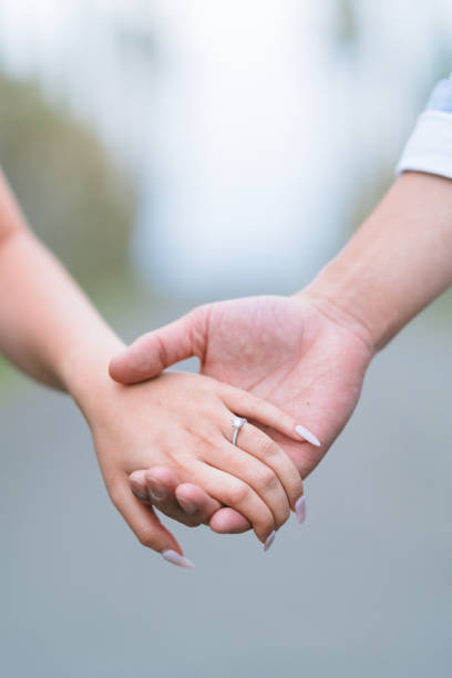 Close-up hands of young couple wearing engagement ring.