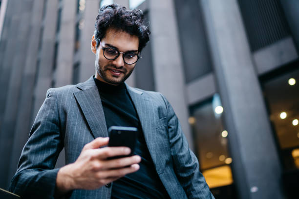 istock Smiling prosperous male entrepreneur reading information from website browsed on cellular outdoors, positive young businessman in formal suit watching video online via mobile phone and 4G internet 1159429986