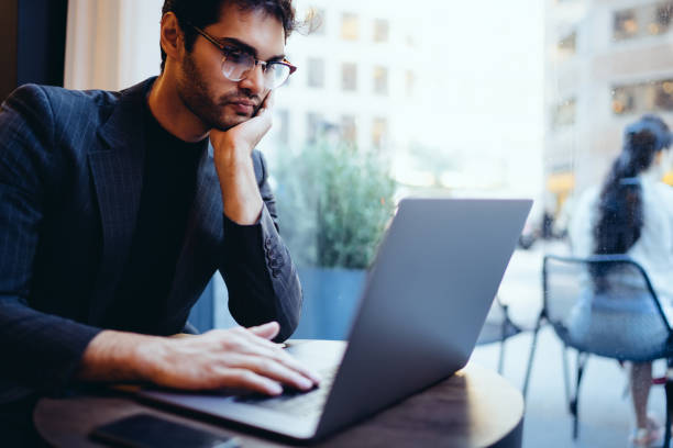 istock Pensive male financial manager searching information data on modern laptop computer connected to wireless 4G internet sitting in coworking space.Young owner checking mail on netbook 1159430199