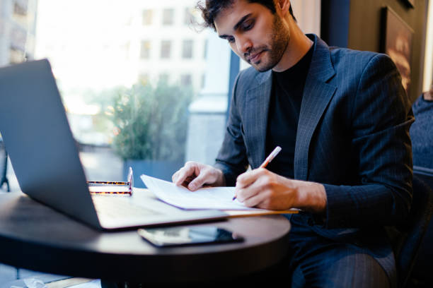 istock Successful young entrepreneur dressed in formal wear writing down financial reports and fill in documents during remotely work at digital netbook connected to wireless 4G internet in stylish cafe 1159430231