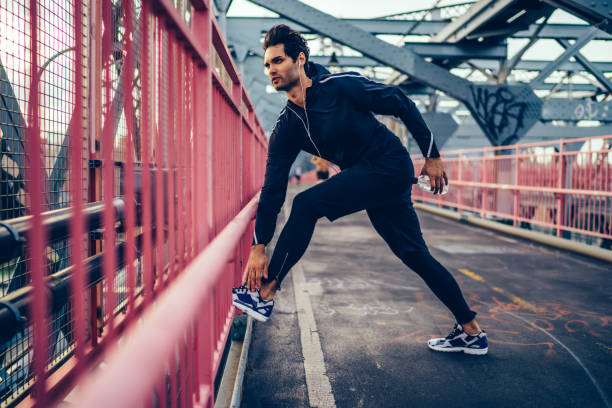 istock Handsome young man dressed in stylish tracksuit doing sport exercises during morning workout on bridge of modern town.Jogger training outdoors.Young athletic man 1159430551