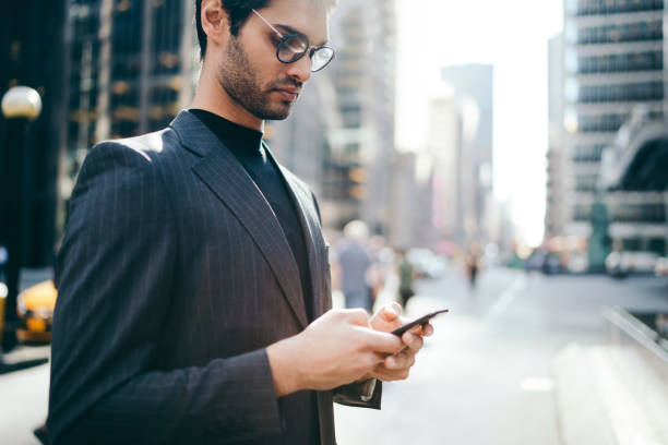 istock Cropped image of confident banker in elegant suit checking mail and sending notification on smartphone via 4G internet standing in urban setting.Pensive financial manager messaging in business chat 1159430765