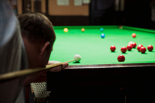 Adult man ready to take a shot in a game of snooker on a pool table.