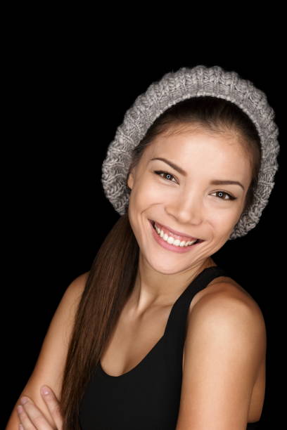 Asian woman modern hipster portrait smiling happy and confident looking at camera isolated on black background wearing knit hat. Multicultural Caucasian Asian female model.