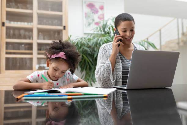 istock Girl doing her homework while mother using laptop and talking on mobile phone 1159436002