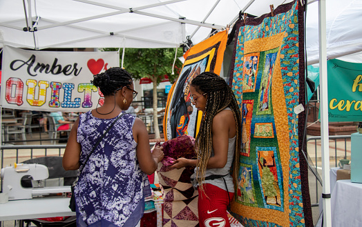 Athens, Georgia - June 22, 2019: A quilt vendor shows a handcrafted quilt to a customer in a booth at the AthFest music and arts festival.
