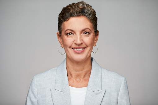 Middle aged sophisticated businesswoman studio headshot, wearing a suit.