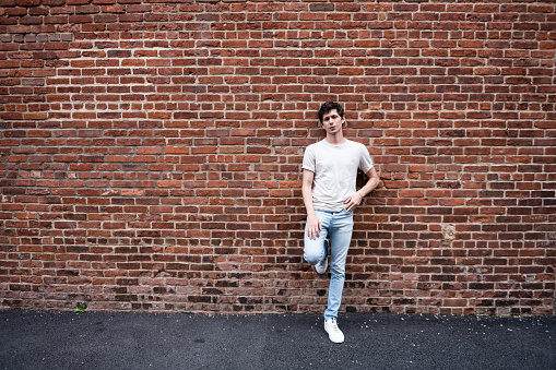 This is a color photograph of a young American man leaning against a red brick wall in Brooklyn, New York USA.