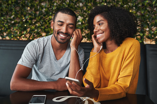 Portrait of an african young couple together listening music in cafe on one earphone