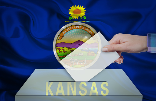 Hand with voting ballot and box in front of the flag KANSAS - USA