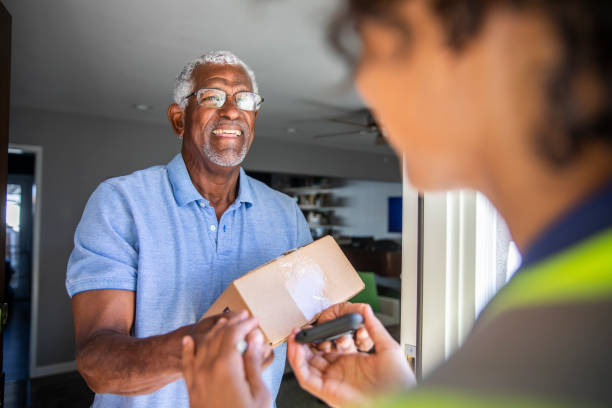 Black Woman Delivers package to customer A young black woman delivers a package to a senior black man receiving stock pictures, royalty-free photos & images