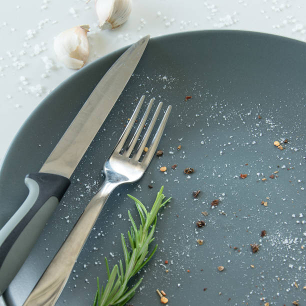 istock Grey empty ceramic plate with herbs knife and fork on salty white background. Minimal design. Space for text or menu 1159447610