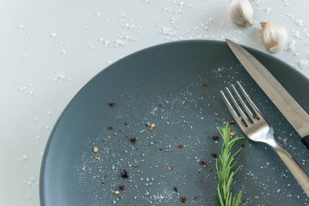 istock Grey empty ceramic plate with herbs knife and fork on salty white background. Minimal design. Space for text or menu 1159447614