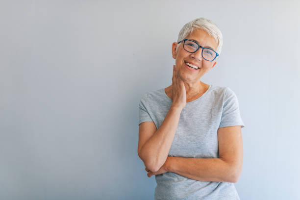 retrato de mujer madura alegre de pie contra la pared gris. - white hair fotografías e imágenes de stock