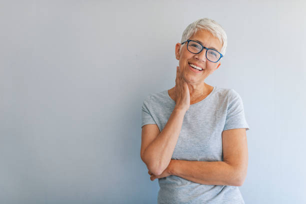 Portrait of cheerful mature woman standing against grey wall. Woman headshot looking at camera. Portrait of beautiful mature woman. Portrait of businesswoman on grey background. Smiling senior woman. gray hair photos stock pictures, royalty-free photos & images