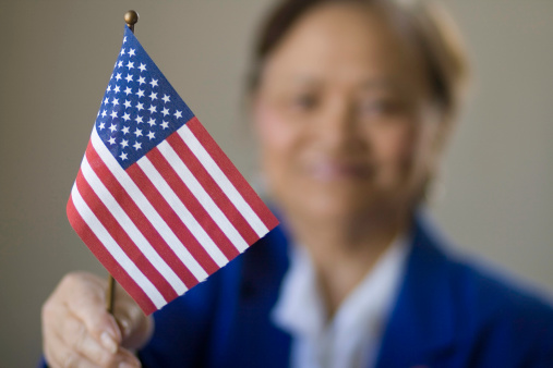 A female Asian proudly holds up the miniature U.S. flag, which is in focus in the foreground, she is given after becoming a U.S. citizen.