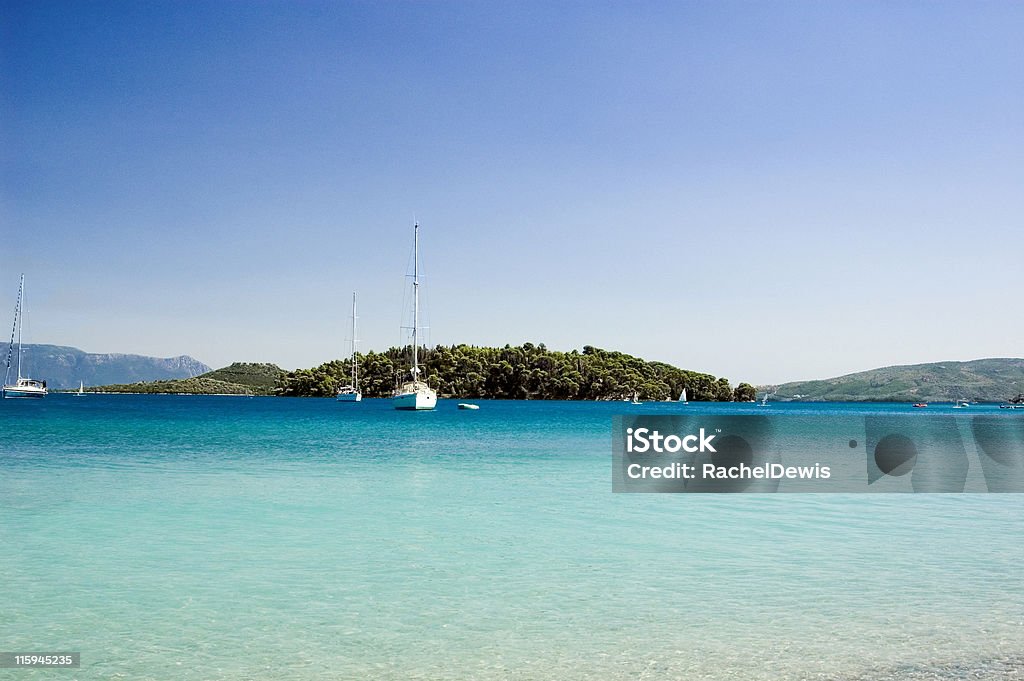 Holiday island Pure blue seas, boats sail away to a wooded island in the distance. Activity Stock Photo