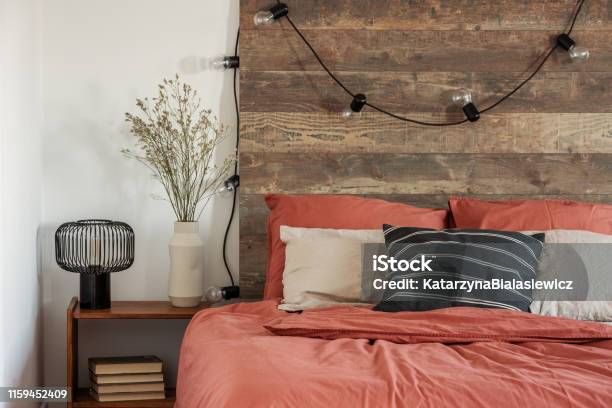 Flowers In Beige Vase And Black Industrial Lamp On Wooden Bedside Table Next To Comfortable Bed With Pillows Stock Photo - Download Image Now