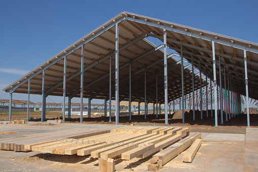 Construction of agricultural facilities. Wooden beams for the construction of the roof against the background of a village hangar under construction