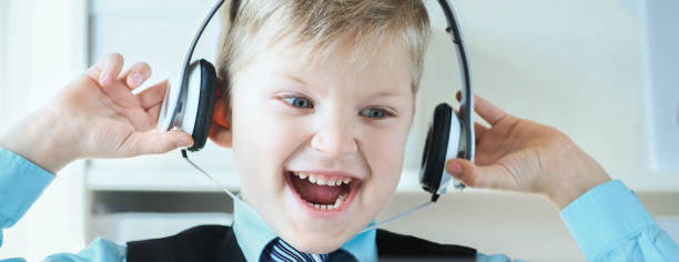 carino bambino di 6 anni in giacca e cravatta che ascolta musica o tutorial audio sulle cuffie sullo sfondo dell'ufficio. - one little boy audio foto e immagini stock