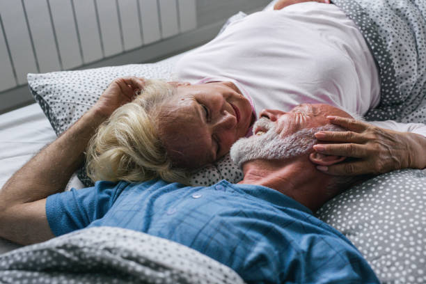 The old senior couple are kissing in bed Senior couple lies in bed. senior man kisses senior woman in the morning sex senior couples stock pictures, royalty-free photos & images