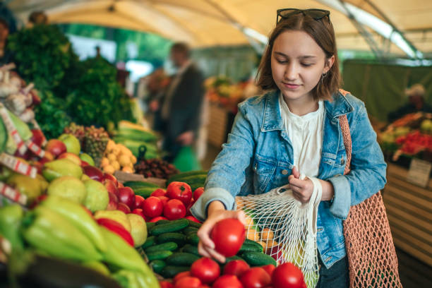 Young girl choosing vegetables and fruit at a farmers market with reusable bag, plastic free and zero waste concept Teenager holding ecologically friendly reusable bag with fruit and vegetables farmers market healthy lifestyle choice people stock pictures, royalty-free photos & images