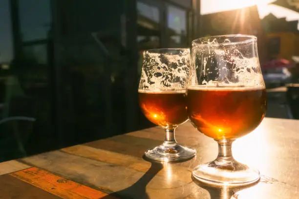 Photo of Closeup of two glasses of beer on terrace table with evening sun shining through them. Relaxation, food and drink concept with copy space.