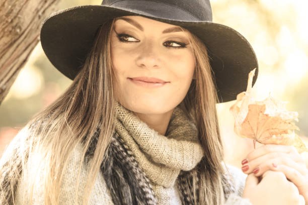 Seasonal specific. Gorgeous lovely young girl holding gold brown leaf. Beauty trendy woman spending time in autumnal park.