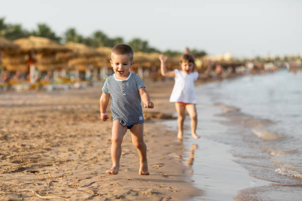 nettes kleines baby mädchen und junge spielen und laufen an einem strand - lifestyles child beach digging stock-fotos und bilder