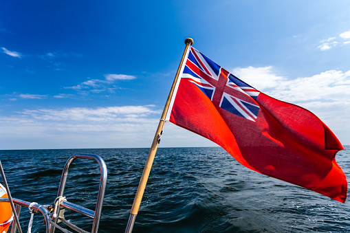 The uk red ensign the british maritime flag flown from yacht sail boat, blue sky and baltic sea. Summer and travel voyage