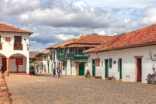Villa de Leyva, Colombia - November 26, 2017: Looking towards the western corner on Carrera 10, in the historic, colonial. Andean Town, in the Boyacá Department. It is as if time has stood still for about 450 years in this Town. Some local people can be seen on the Carrera; in the far backgound are the Andes Mountains. Founded in 1572 and located at an altitude of just over 7000 feet above mean sea level on the Andes, the whole town was declared a National Monument by the Colombian Government in 1954 to protect its colonial architecture and heritage. Photo shot in the morning sunlight; horizontal format. Copy space.