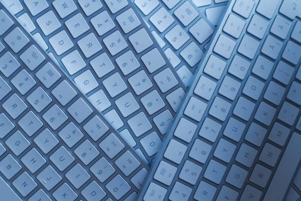 closeup of computer keyboards on a black dark desk top view macro closeup of many white wireless aluminum computer keyboards on top of each other on a dark black desk with natural light enter key computer keyboard computer key white stock pictures, royalty-free photos & images