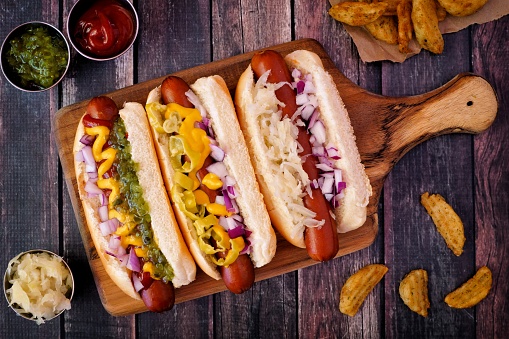 Hot dogs fully loaded with assorted toppings on a paddle board, overhead scene