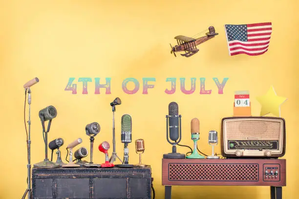 Photo of Retro microphones, wooden plane and USA flag, old radio, calendar, star front yellow background with 4th of July date text. Independence day congratulations greeting card. Vintage style filtered photo